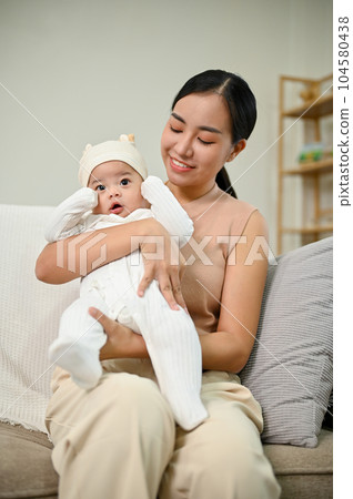 Beautiful Asian Mother holding her baby boy while relaxing on the sofa 104580438