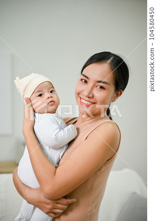 Beautiful Asian Mother holding her baby boy while relaxing on the sofa Beautiful Asian Mother holding her baby boy while relaxing on the sofa 104580450