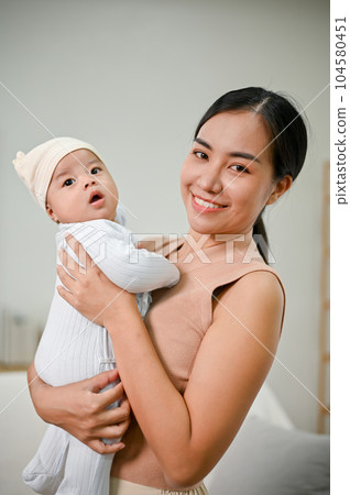 Beautiful Asian Mother holding her baby boy while relaxing in the living room Beautiful Asian Mother holding her baby boy while relaxing in the living room 104580451