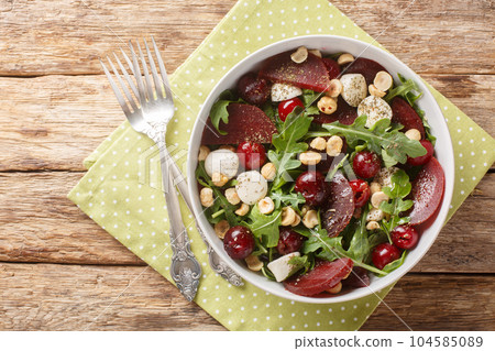 Dietary vegetable berry salad of arugula, beets, cherry berries, cheese, hazelnuts close-up in a bowl. Horizontal top view Dietary vegetable berry salad of arugula, beets, cherry berries, cheese, hazelnuts close-up in a bowl. Horizontal top view 104585089