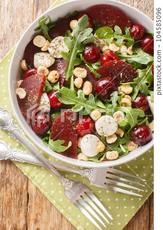Portion of delicious salad of arugula, beetroot, cherry berries, cheese, hazelnuts close-up in a bowl. Vertical top view 104585096