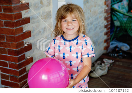 Smiling little child playing with balloon at home. Lifestyle, indoor game for children. Happy preschool girl in pajamas. Smiling little child playing with balloon at home. Lifestyle, indoor game for children. Happy preschool girl in pajamas. 104587132