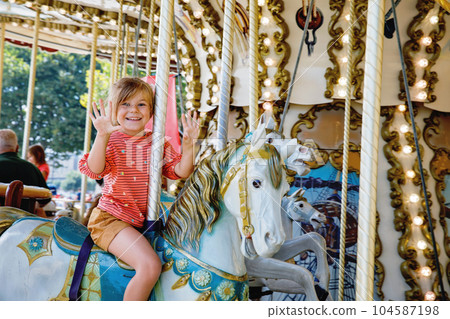 Happy positive preschool girl having a ride on the old vintage merry-go-round in city of St Malo France. Smiling child on a horse. 104587198
