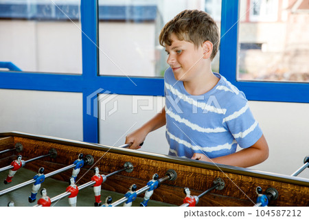 Smiling school boy playing table soccer. Happy excited child having fun with family game with siblings or friends. Positive kid. 104587212
