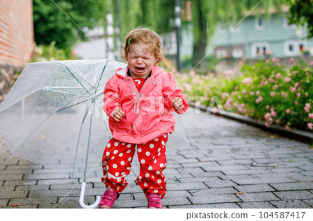 Cute adorable crying sad toddler girl on a walk. Little baby child going for walk with parents. frustrated healthy kid in rain clothes cry, unhappy and hungry. 104587417