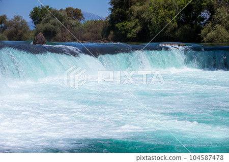 Manavgat waterfall Manavgat River is near the city of Side, 3 km north of Manavgat in Turkey. A wide stream of water falls from a low height. 104587478