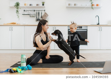 Female giving high five to dog near baby on yoga mat at home Female giving high five to dog near baby on yoga mat at home 104594393