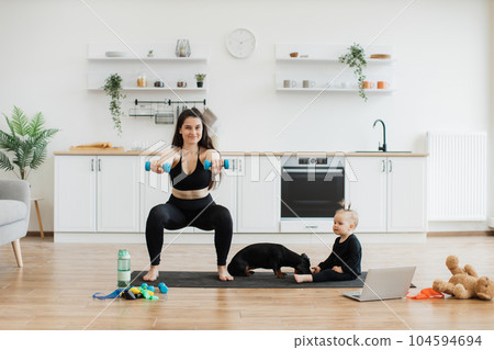 Mom doing squats with weights near baby with pet on floor Mom doing squats with weights near baby with pet on floor 104594694
