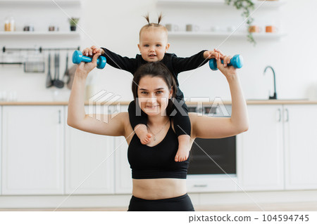 Female parent holding baby with weights around neck indoors 104594745