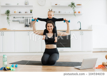 Mom carrying baby with dumbbells on shoulders while sitting 104594839