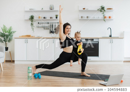Lady doing walking lunges with kid on knee in kitchen Lady doing walking lunges with kid on knee in kitchen 104594883