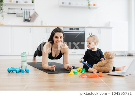 Lady in plank pose helping baby with resistance band for toy 104595781