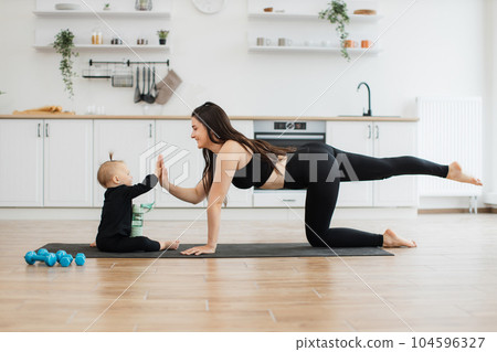 Kid responding to high-five gesture from mom on yoga mat 104596327