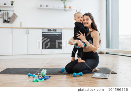 Female parent with dumbbell hugging baby on kitchen floor 104596336