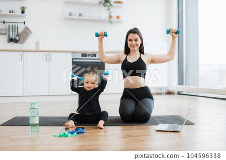 Mother and infant lifting dumbbells while sitting on floor 104596338
