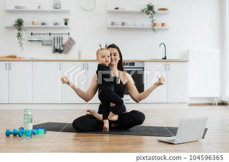Girl joining mom during online yoga class via device indoors Girl joining mom during online yoga class via device indoors 104596365