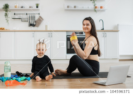 Mom with resistance band training near baby on room floor 104596371