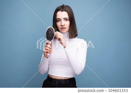 A brunette with a comb in her hands is worried about hair loss. Studio portrait blue background 104601353