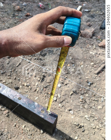 Builder is using a tape measure to find the distance between the ground and the mold to find the correct 104602655
