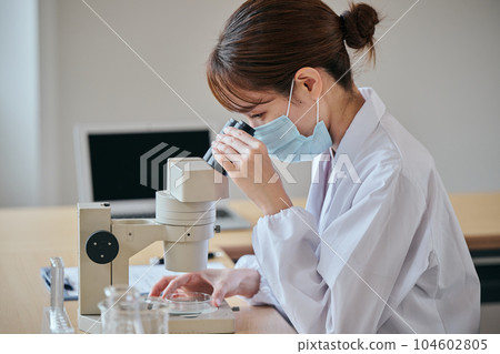 一位身穿白大褂的年輕女子透過顯微鏡鏡頭觀察 一位身穿白大褂的年輕女子透過顯微鏡鏡頭觀察 104602805