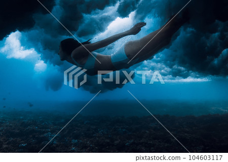 Woman swim under breaking wave with foam in transparent ocean. Duck dive without surfboard Woman swim under breaking wave with foam in transparent ocean. Duck dive without surfboard 104603117