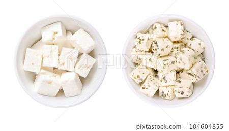 Greek feta cubes, brined cheese, in white bowls. Cheese, matured in brine, with soft, moist texture, and fresh, salty, acidic taste, cut into cubes. Pure (left), and with Mediterranean herbs (right). 104604855