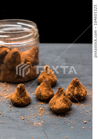 Truffle chocolates in cocoa in a glass jar and laid out on a black background 104605325