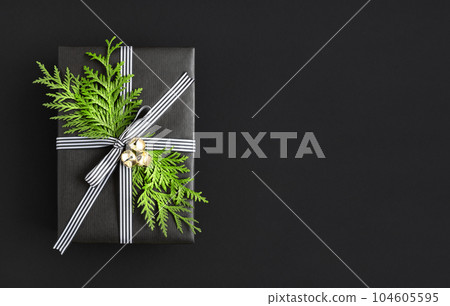 Black gift box with sprig of thuja and bells on black background. Space for your text. Black gift box with sprig of thuja and bells on black background. Space for your text. 104605595