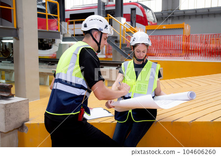 Young caucasian engineer man and woman or worker looking blueprint and checking electric train. Young caucasian engineer man and woman or worker looking blueprint and checking electric train. 104606260