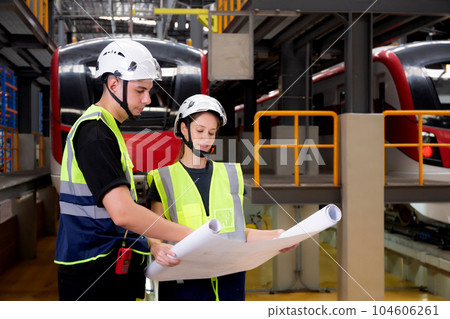 Young caucasian engineer man and woman or worker looking blueprint and checking electric train. 104606261