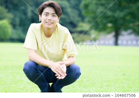 Young man crouching on grass listening to music 104607506