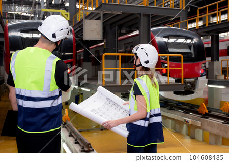 Young caucasian engineer man and woman or worker looking blueprint and checking electric train. 104608485