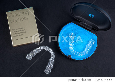 Invisible retainers case with orthodontic aligner brackets top view. Black plastic dental container for invisalign braces and cleaning crystals for them. 104608537