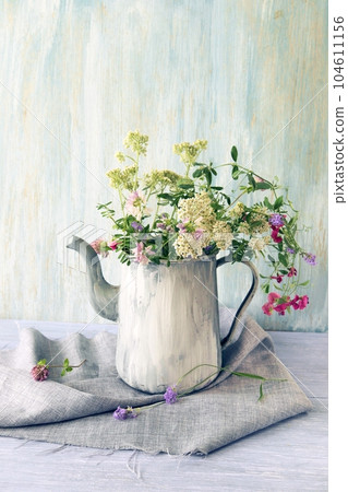 Fresh meadow flowers in an old jug on a wooden table, a bouquet of flowers, summer, autumn season 104611156