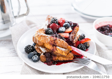 Stack of freshly made french toast garnished with mix berry compote and powder sugar. Stack of freshly made french toast garnished with mix berry compote and powder sugar. 104611750