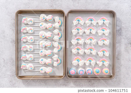 Flat lay. Unbaked unicorn theme meringue pops on a baking sheet lined with parchment paper. Flat lay. Unbaked unicorn theme meringue pops on a baking sheet lined with parchment paper. 104611751