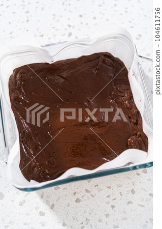 Pouring fudge mixture into the baking pan lined with parchment paper to prepare chocolate fudge with peanut butter swirl. Pouring fudge mixture into the baking pan lined with parchment paper to prepare chocolate fudge with peanut butter swirl. 104611756