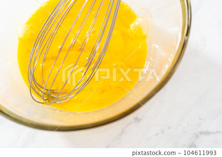 Mixing wet ingredients in a large glass mixing bowl to bake lemon blueberry bundt cake. Mixing wet ingredients in a large glass mixing bowl to bake lemon blueberry bundt cake. 104611993