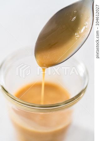 Spooning eggnog caramel sauce from the glass jar. Spooning eggnog caramel sauce from the glass jar. 104612027