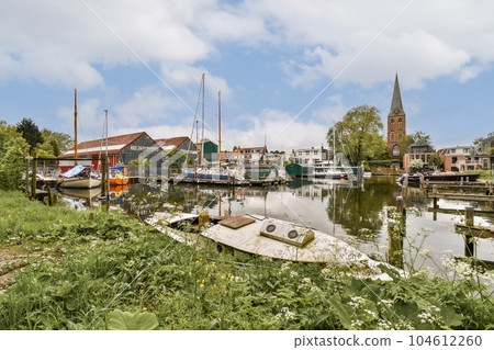 boats in the water and buildings on the other side of the river, with green vegetation growing all around it 104612260