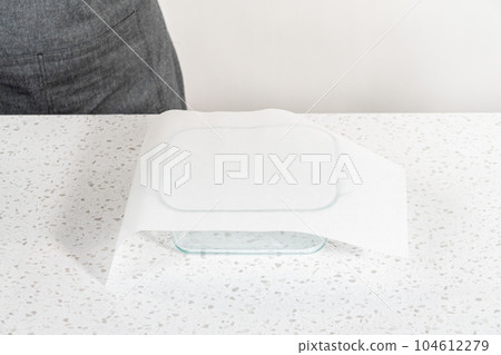 Lining glass baking pan with parchment paper sheet to prepare chocolate peanut butter fudge. Lining glass baking pan with parchment paper sheet to prepare chocolate peanut butter fudge. 104612279