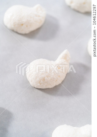 Piping meringue from the piping bags with the metal tip into parchment paper to bake meringue cookies. 104612297