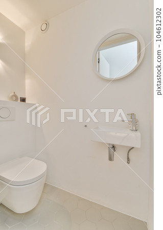 a white bathroom with a toilet and sink in front of a round mirror on the wall behind it is a small window a white bathroom with a toilet and sink in front of a round mirror on the wall behind it is a small window 104612302