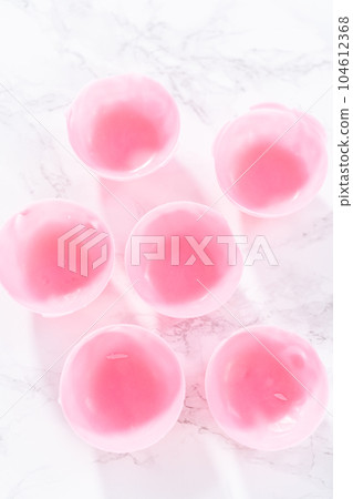 Removing pink chocolate shells from the silicone chocolate molds with melted pink chocolate to prepare hot chocolate bombs. Removing pink chocolate shells from the silicone chocolate molds with melted pink chocolate to prepare hot chocolate bombs. 104612368