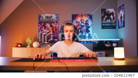Teenage gamer in headphones speaks into microphone, plays online video game on computer Teenage gamer in headphones speaks into microphone, plays online video game on computer 104612467