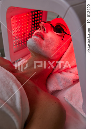 Woman getting facial treatment with led therapy. 104612490