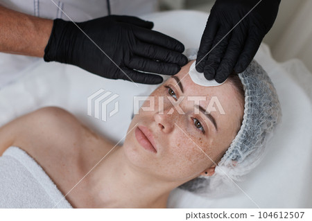 beautician cleanses skin of woman with cotton sponge. . 104612507