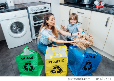 Mother is teaching kid how to recycle help the boy aware environmental importance - mom educates son sort garbage into different bins on kitchen. Family sorting garbage at home. Concept of recycling. 104612585