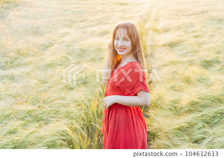 Young happy woman in red dress walking in wheat field on sunset. Breathe of freedom. Positive emotions feeling life, peace of mind. Mental health practice. Nature relaxation. Soft selective focus 104612613