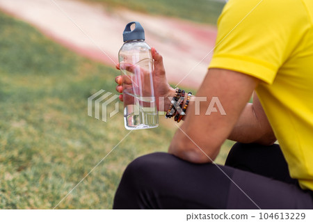 The athlete, taking a break, rests at the sports arena, holding his water bottle, The athlete, taking a break, rests at the sports arena, holding his water bottle, 104613229